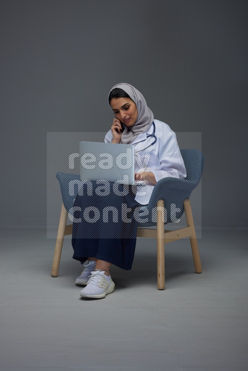 A doctor wearing a light gray head scarf sitting on blue chair on grey background