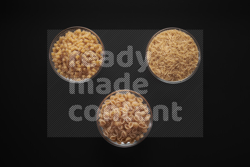 Different pasta types in glass bowls on black background