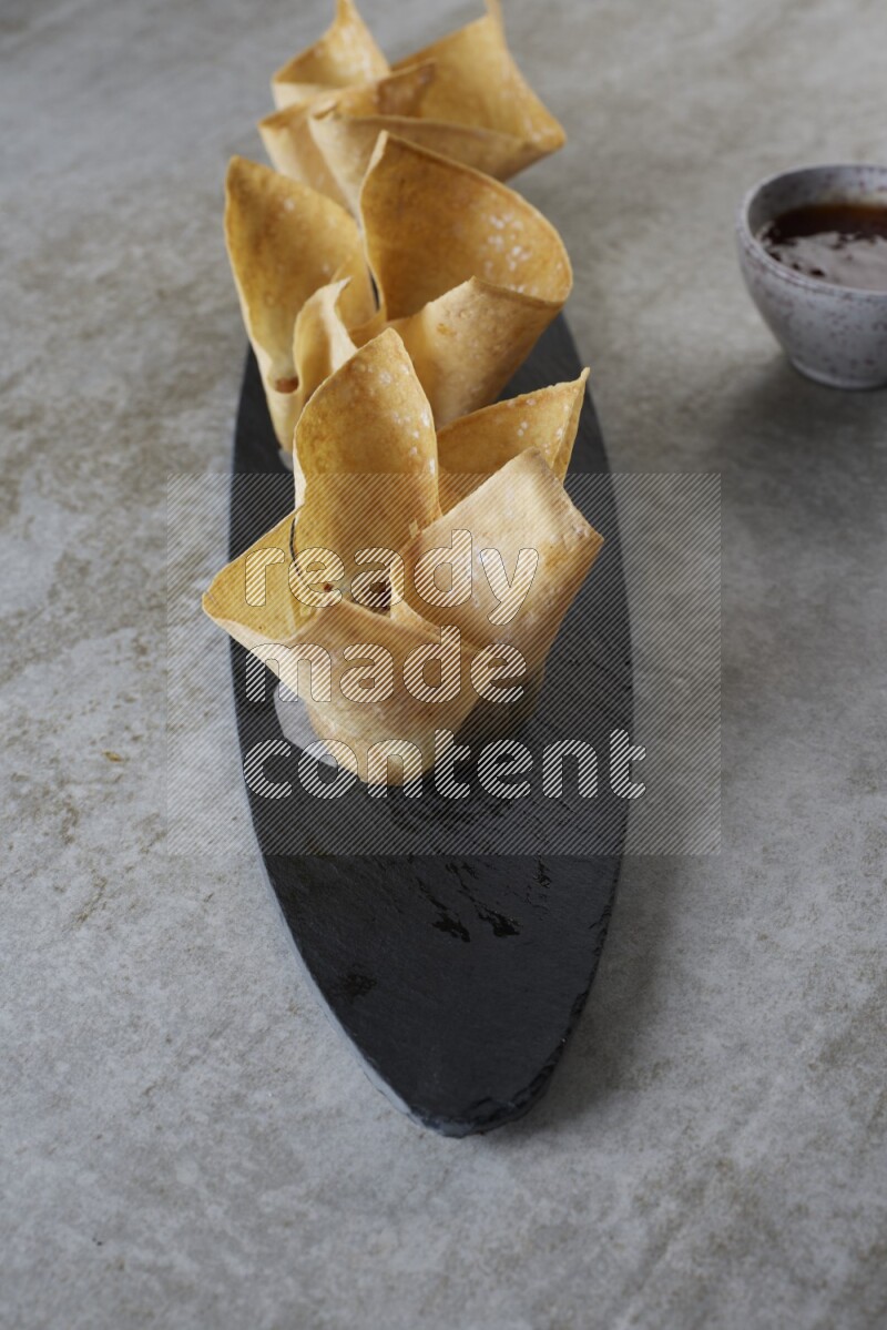 wonton cups with soy sauce ramkin on oval slate on grey textured counter top