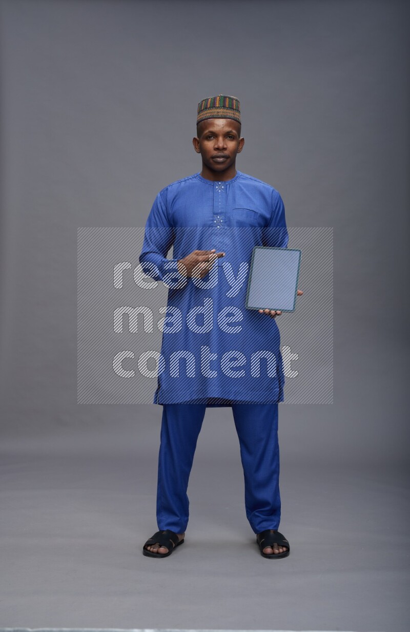 Man wearing Nigerian outfit standing showing tablet to camera on gray background