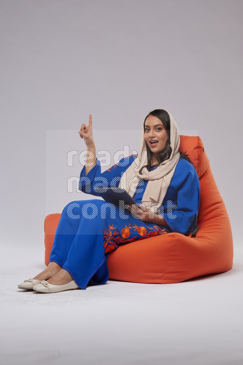 A Saudi woman sitting on an orange beanbag and working on tablet