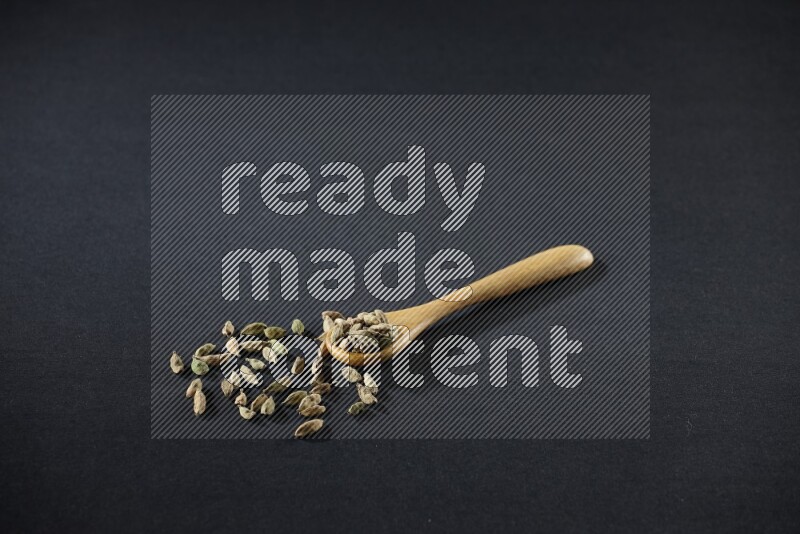 ملعقة خشبية ممتلئة بالهيل على خلفية سوداء