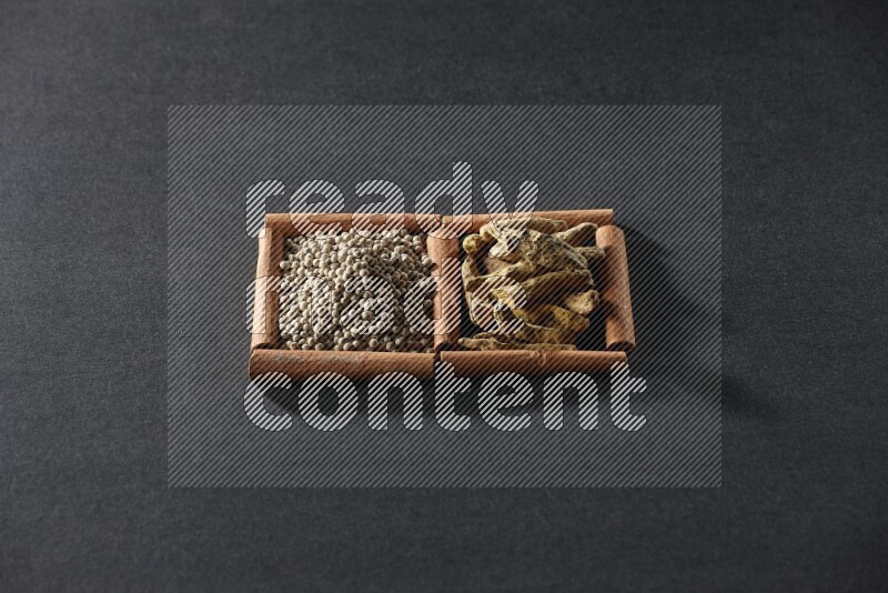 مربعان من أعواد القرفة ممتلئان بحبوب الفلفل الأبيض وأصابع الكركم علي خلفية سوداء