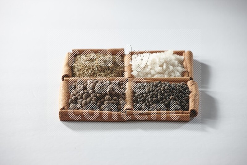 4 مربعات من أعواد القرفة ممتلئة بالكمون والملح الأبيض وبهار الفلفل الحلو وحبوب الفلفل الأسود على أرضية بيضاء