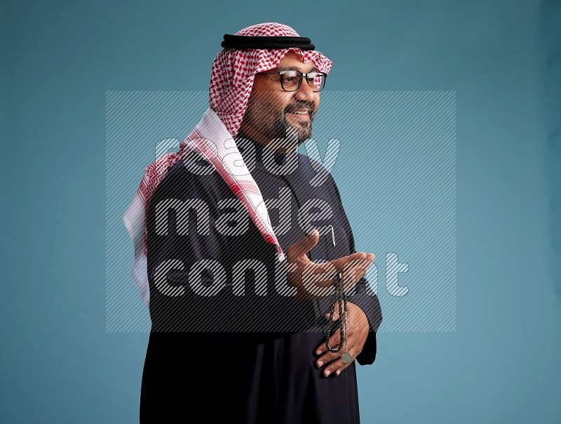 Saudi Man with shimag Standing Interacting with the camera on blue background