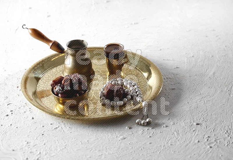 Dates in a metal bowl with coffee and prayer beads on a tray in a light setup