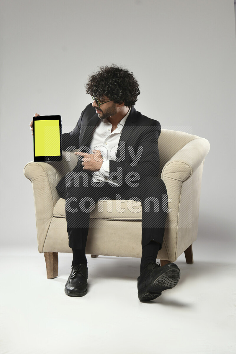 رجل يرتدي ملابس رسمية يجلس علي كرسي و يحمل تابلت علي خلفية بيضاء