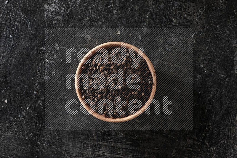 A wooden bowl full of cloves on a black flooring