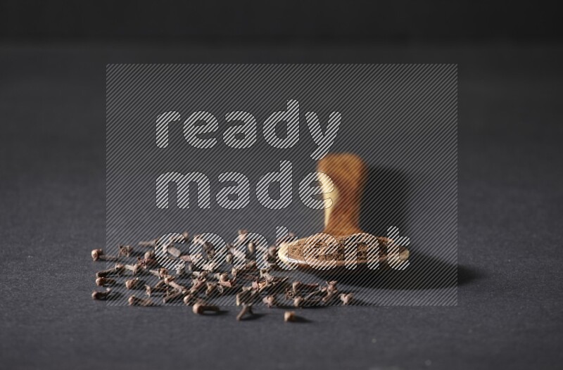 مغرفة خشبية ممتلئة ببودرة القرنفل مع بعض حبوب القرنفل الكاملة حولها على خلفية سوداء