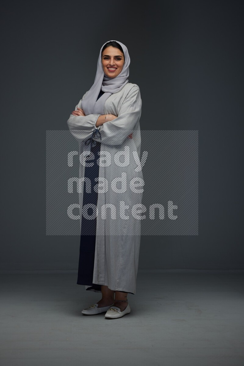 A Saudi woman wearing a light gray Abaya and head scarf standing and making multi poses eye level on a grey background