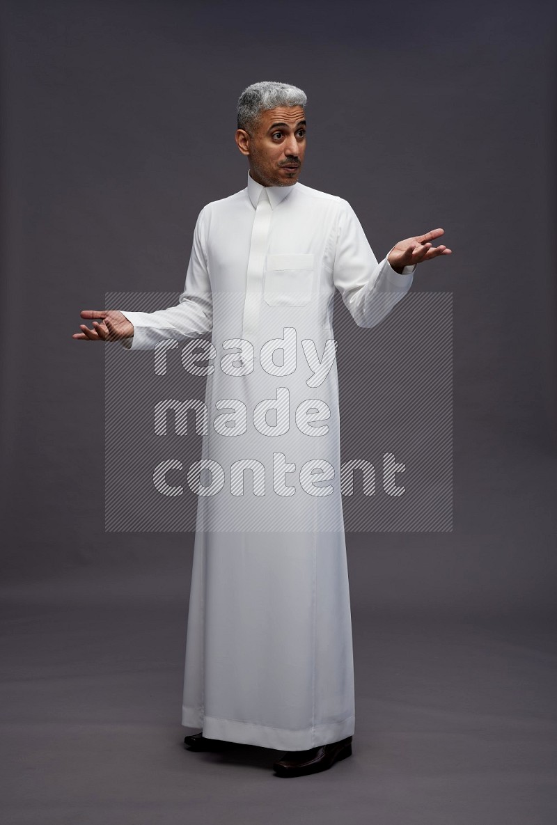 Saudi man wearing thob standing interacting with the camera on gray background