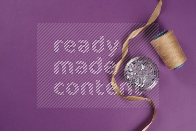 مجموعة من أدوات الخياطة والتفصيل باللون البيج على خلفية أرجوانية