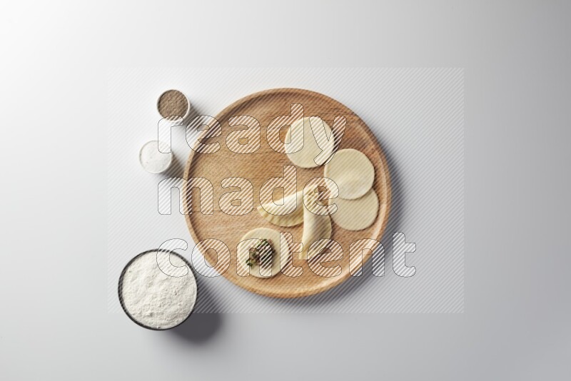 two closed sambosas and one open sambosa filled with meat while flour, salt, and black pepper aside in a wooden dish on a white background