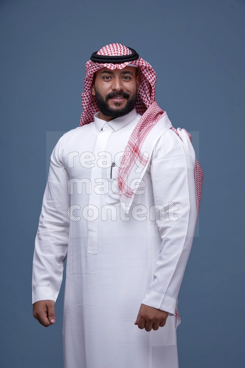 A Saudi man posing on blue background wearing Thob and Shomag