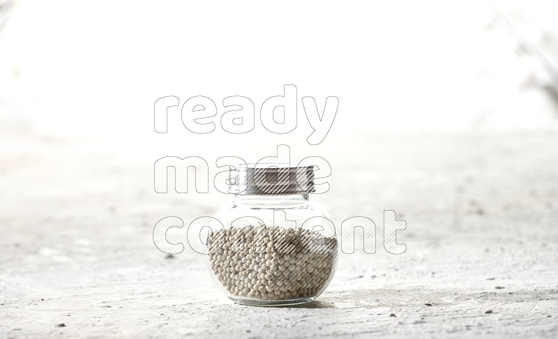 Herbal Glass jar full of white pepper beads on textured white flooring