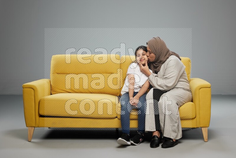 A girl with her mother sitting and interacting with the camera on gray background