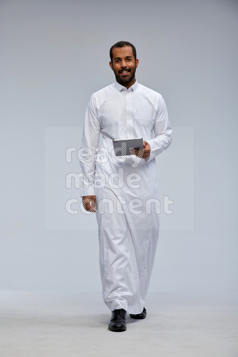 Saudi man wearing Thob standing working on tablet on Gray background
