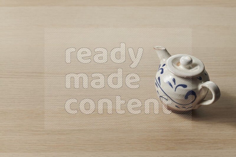A pottery teapot on light wooden background