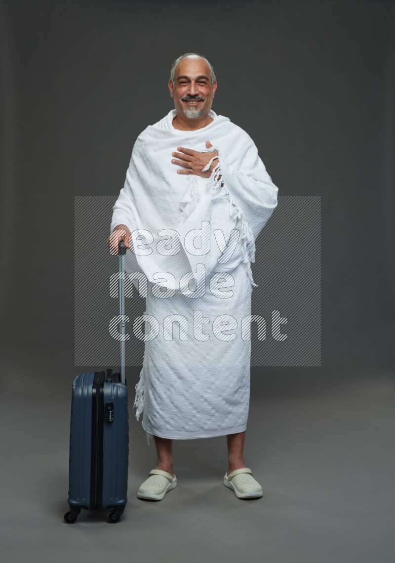 A man wearing Ehram Standing holding traveling bag on gray background