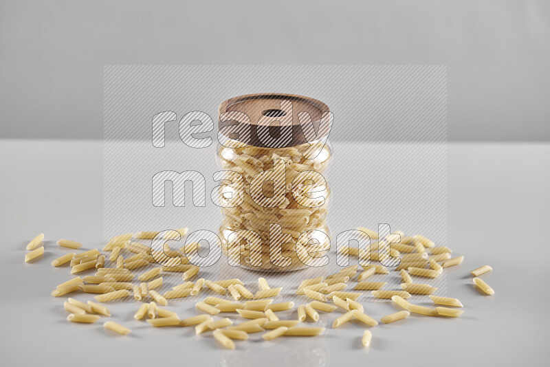 Raw pasta in a glass jar on light grey background