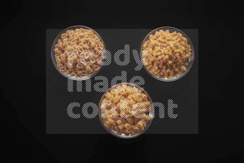 Different pasta types in glass bowls on black background