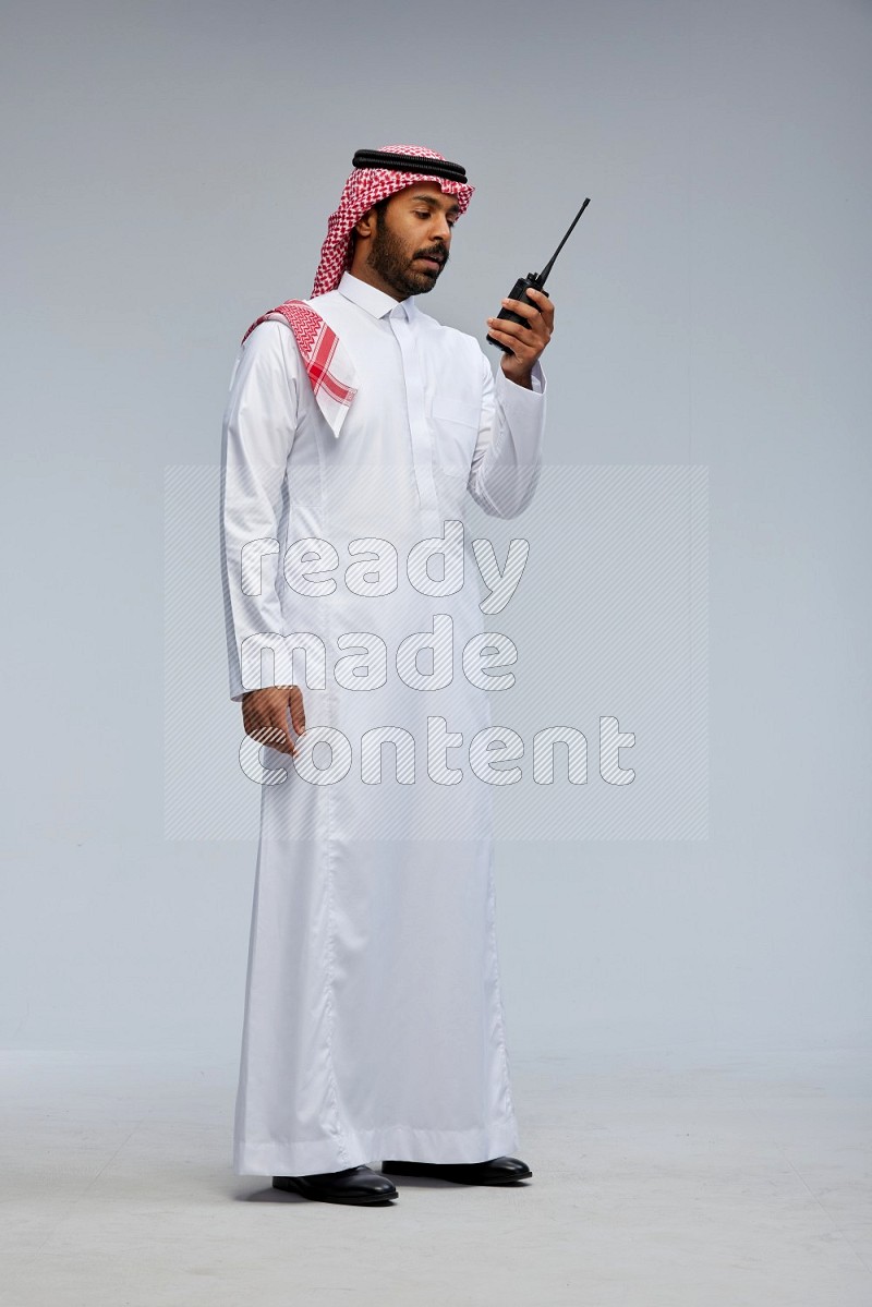 Saudi man Wearing Thob and shomag standing holding walkie-talkie on Gray background