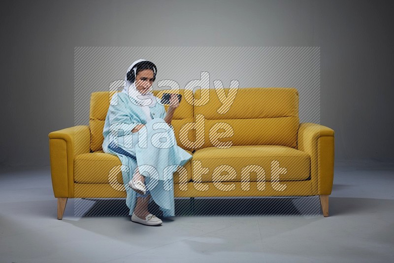 A Saudi woman sitting on a yellow Sofa Watching a Movie wearing Blue Abaya