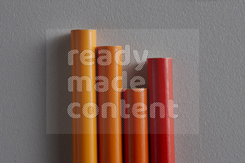 A collection of colored pencils arranged showcasing a gradient of orange hues on grey background