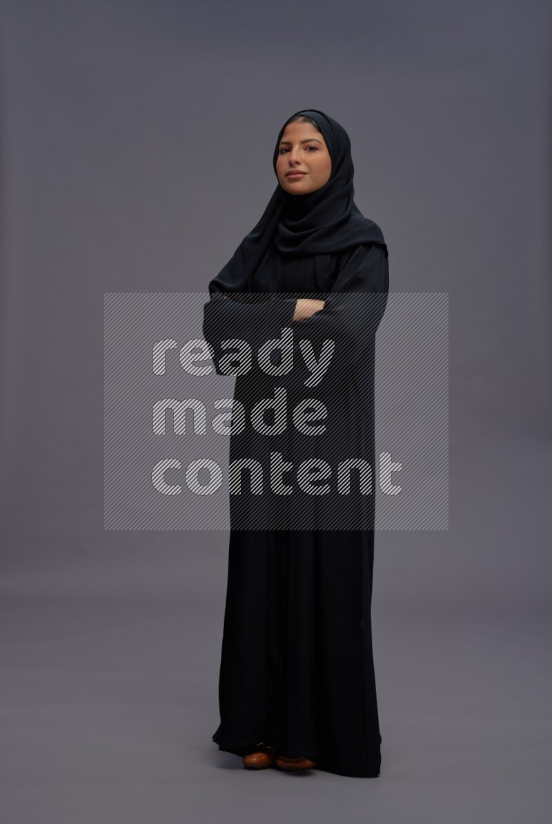 Saudi woman wearing Abaya standing with crossed arms on gray background