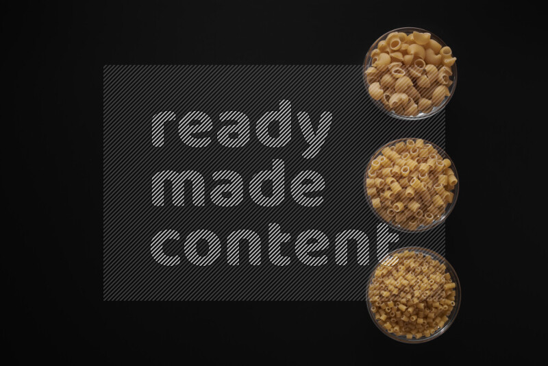 Different pasta types in 3 glass bowls on black background