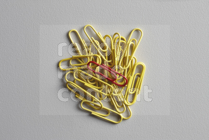 A red paperclip surrounded by bunch of yellow paperclips on grey background