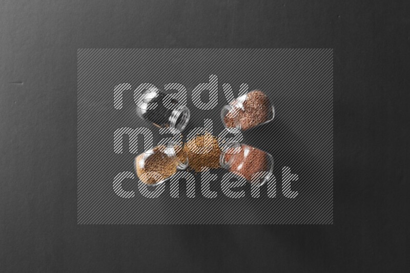 4 glass spice jars full of black seeds, mustard seeds, flax and garden cress on black flooring