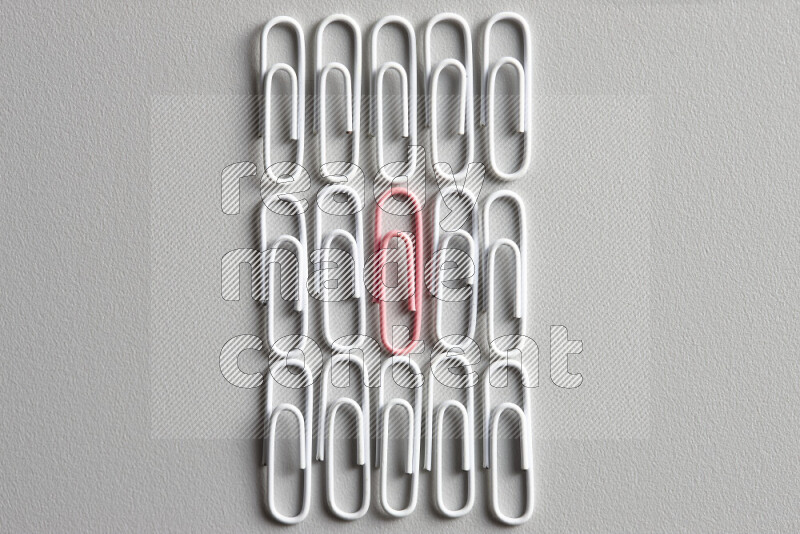 A pink paperclip surrounded by bunch of white paperclips on grey background