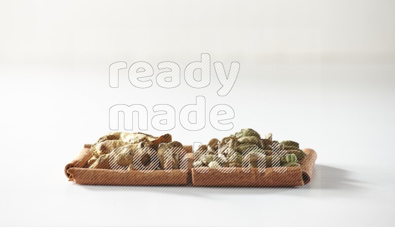 مربعان من أعواد القرفة ممتلئان بحبوب الهيل وأصابع الكركم علي خلفية بيضاء