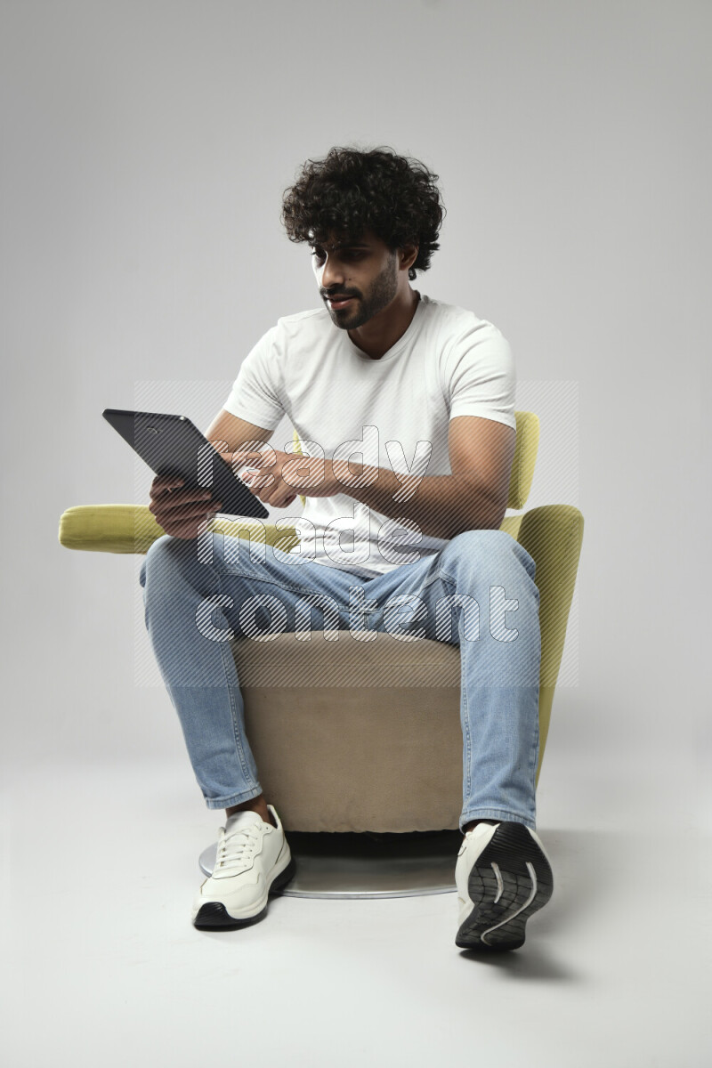 A man wearing casual sitting on a chair browsing on a tablet on white background