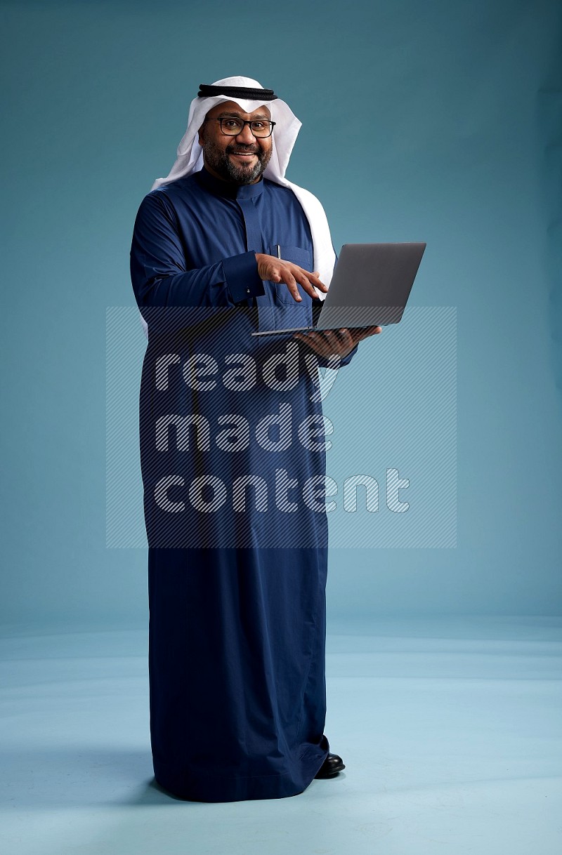 Saudi Man with shimag Standing working on laptop on blue background