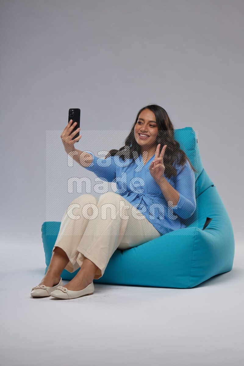 A woman sitting on a blue beanbag and taking selfie