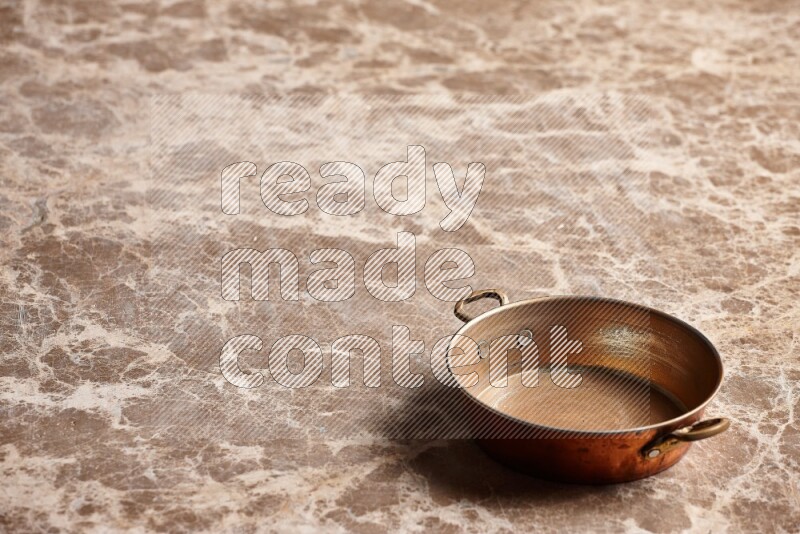 A small copper pan on beige marble background