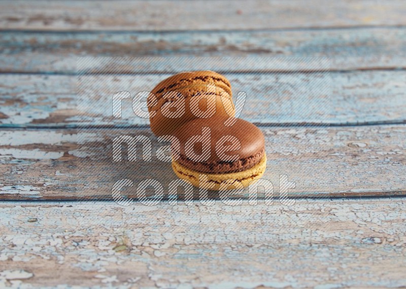 45º Shot of of two assorted Brown Irish Cream, and Yellow, and Brown Chai Latte macarons  on light blue background