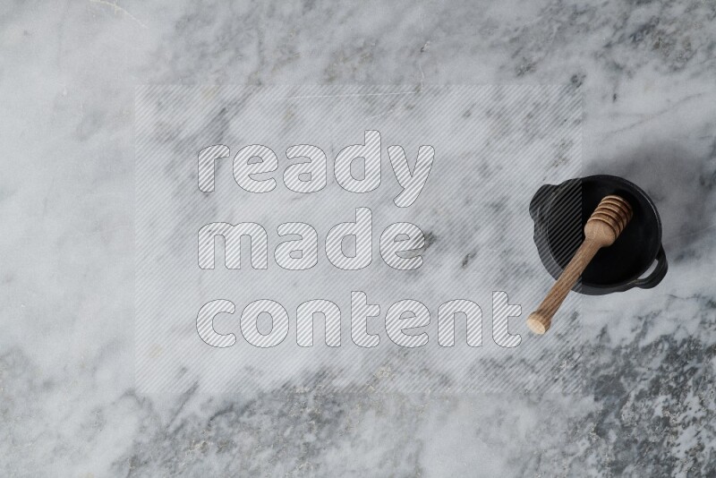 وعاء فخاري أسود مع ملعقة عسل خشبية بداخله على خلفية من الرخام الرمادي