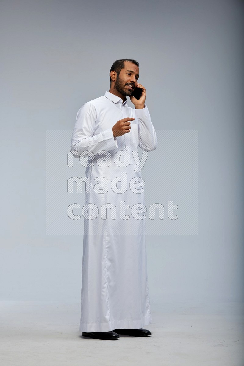 Saudi man wearing Thob standing talking on phone on Gray background