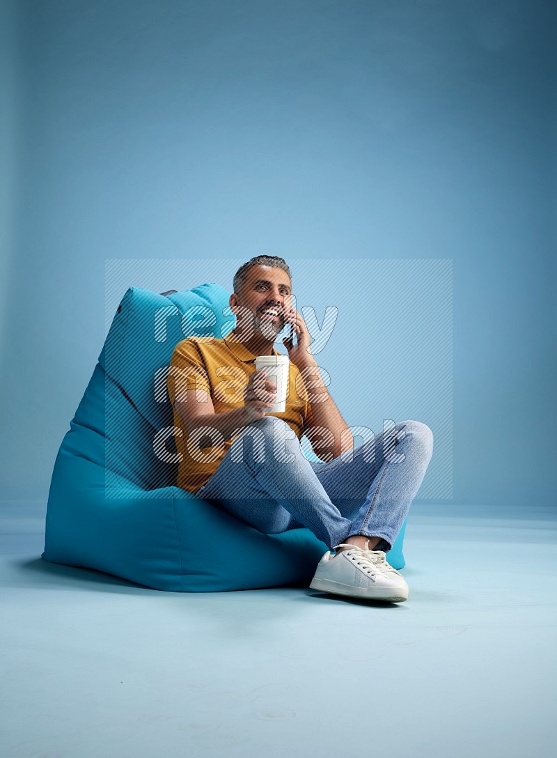 A man sitting on a blue beanbag and drinking coffee