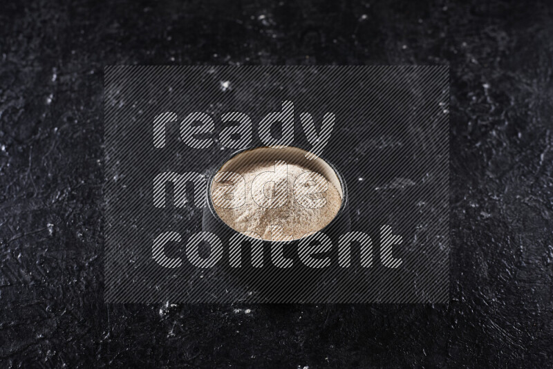 وعاء فخاري اسود ممتلئ ببودرة البصل علي خلفية سوداء