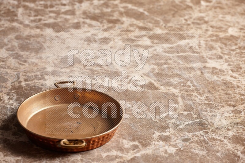 A small copper pan on beige marble background