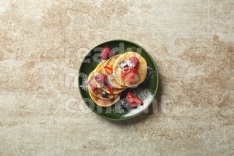 Five stacked mixed berries mini pancakes in a green plate on beige background