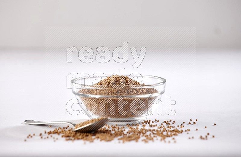 A glass bowl and metal spoon full of mustard seeds on a white flooring in different angles