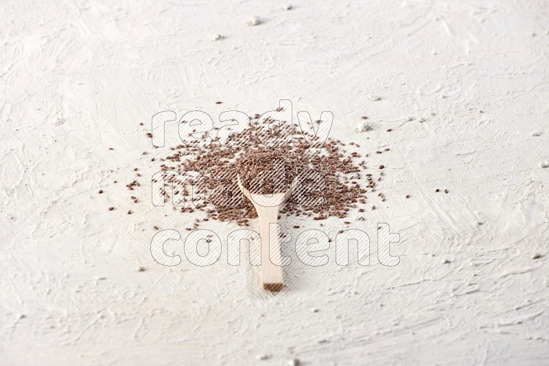 A wooden spoon full of flax seeds surrounded by flax seeds on a textured white flooring
