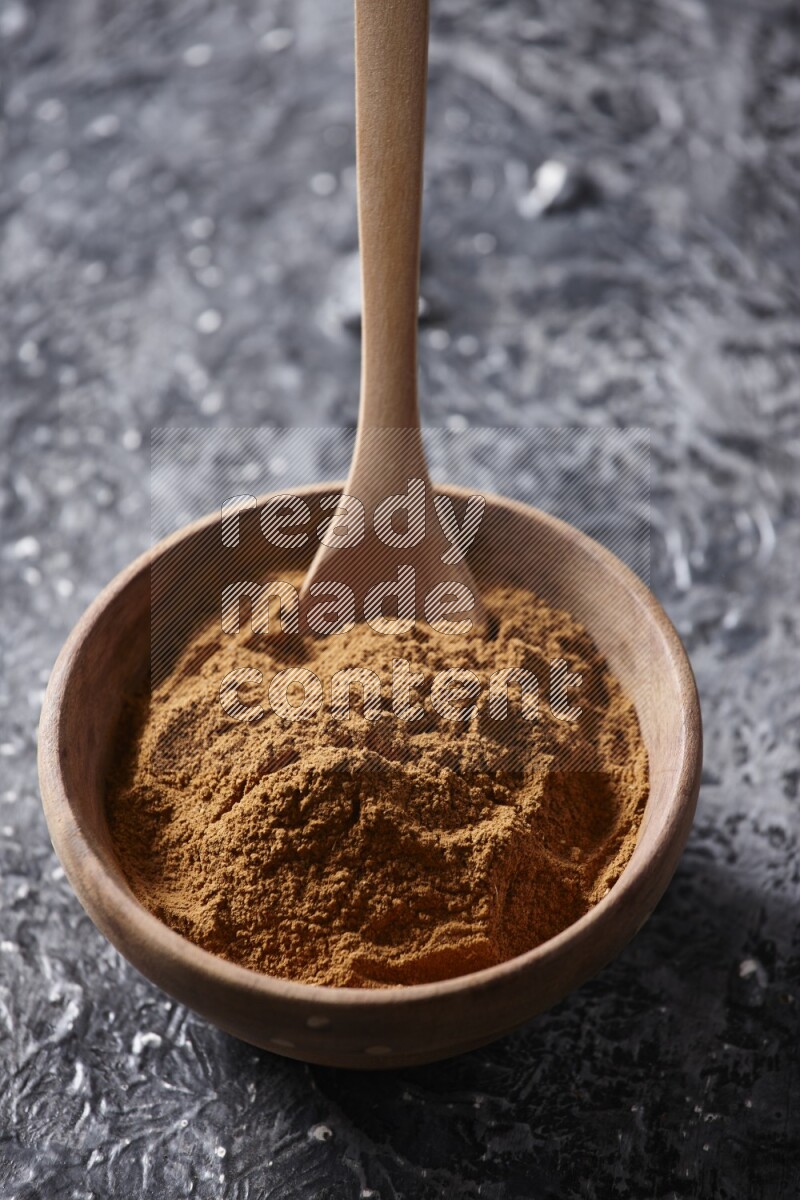 Wooden bowl full of cinnamon powder with a wooden spoon on a textured black background in different angles