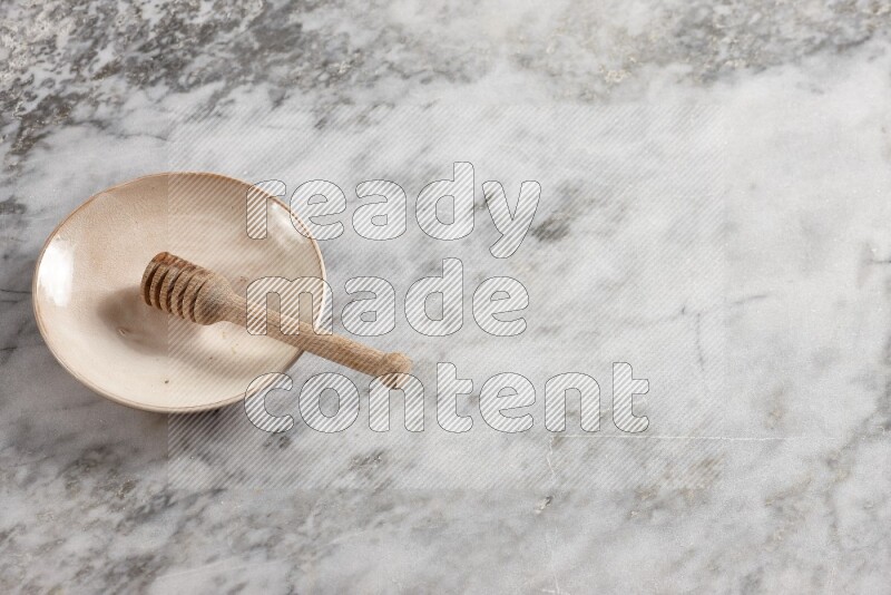 Beige pottery plate with wooden honey dipper in it on grey marble background