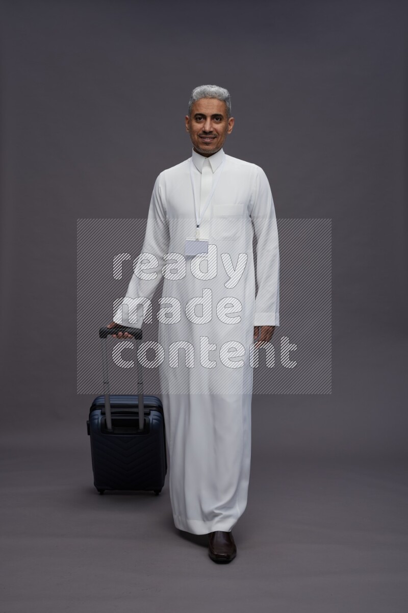 Saudi man wearing thob with neck strap employee badge standing holding bag on gray background